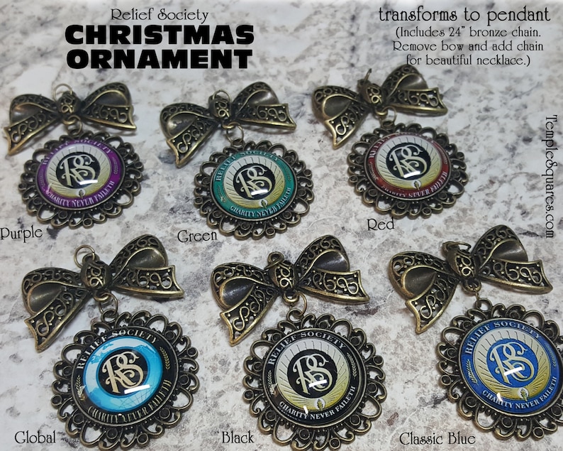 May include: Six different colored Christmas ornaments with a gold filigree design. Each ornament features a gold 'RS' logo with the words 'Relief Society' and 'Charity Never Faileth' around the logo. The ornaments are available in purple, green, red, blue, black, and global.