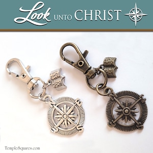 May include: Two silver and bronze compass keychains with a book charm. The silver keychain has a compass with a star in the center and the words "N", "S", "E", and "W" around the edge. The bronze keychain has a compass with a star in the center and the words "N", "S", "E", and "W" around the edge. Both keychains have a book charm with the words "Look unto Christ" on the front.