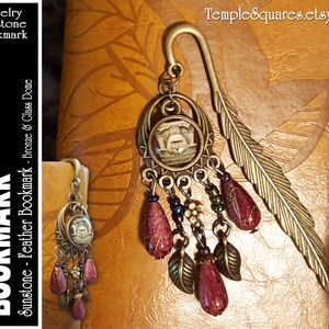 May include: A bronze feather bookmark with a sunstone and glass dome charm. The charm features a decorative design and is accented with red, green, and gold beads.