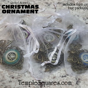 May include: Four gold-colored Christmas ornaments with a blue and green design featuring the text "Relief Society" and the number "18" in a circle. The ornaments are packaged in white organza bags. The text "includes free organza bag packaging" is visible in the image.