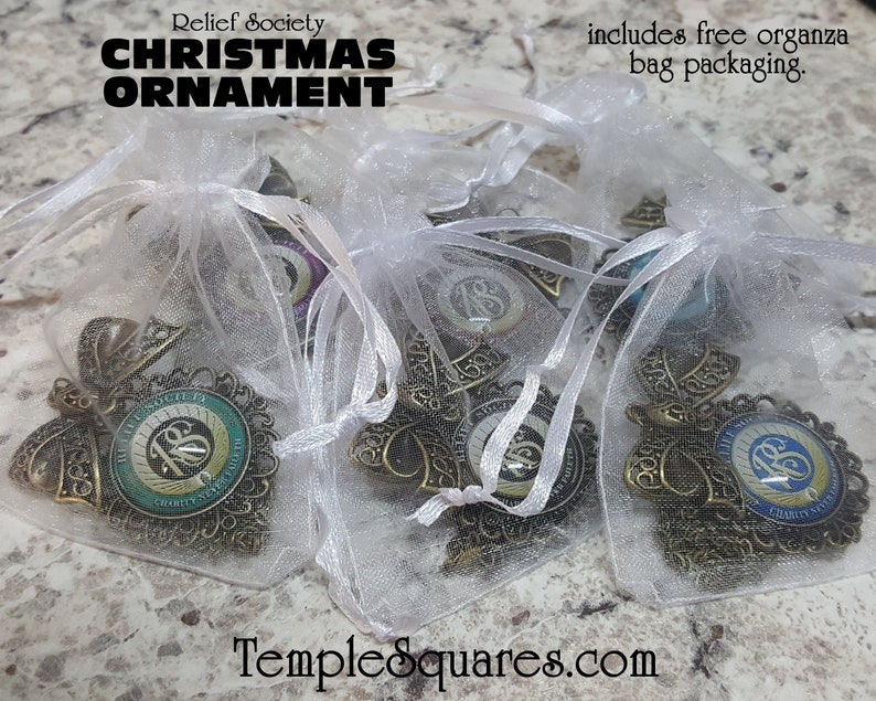 May include: Four gold-colored Christmas ornaments with a blue and green design featuring the text "Relief Society" and the number "18" in a circle. The ornaments are packaged in white organza bags. The text "includes free organza bag packaging" is visible in the image.