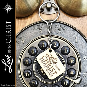 May include: A wooden keychain with the text "Look unto Christ" and the words "Doubt not-Fear not" on a rotary phone dial. The keychain is attached to a silver key ring.