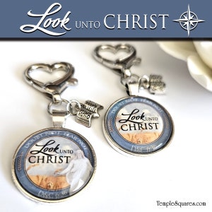 May include: Two silver keychains with heart-shaped clasps and round pendants. The pendants feature the text "Look Unto Christ" and an image of Jesus. Each keychain has a small charm. The text "Doubt Not, Fear Not" is also visible.