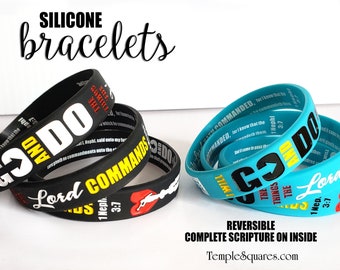 Könnte beinhalten: Zwei Stapel Silikonarmbänder mit religiösem Text. Der obere Stapel ist schwarz mit weißem und gelbem Text. Der untere Stapel ist türkis mit schwarzem und gelbem Text. Der Text auf den Armbändern lautet "Go and Do", "The Things The Lord Hath Commanded", "1 Nephi 3:7", und "Go and Do", "The Things The Lord Hath Commanded", "1 Nephi 3:7".