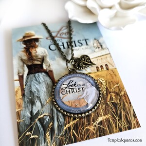 May include: A bronze necklace with a round pendant featuring a blue and white image of a woman with the text "Look unto Christ" and the scripture reference "D&C 6:36". The pendant is surrounded by a decorative bronze frame.