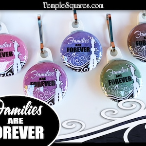 May include: Five zipper pulls with round, colorful buttons featuring the text "Families are Forever" in black lettering. The buttons have a white floral design and a silhouette of a person standing on a building.