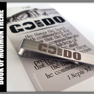 May include: A silver tie clip with the words "Go and Do" engraved in brown lettering. The tie clip is on top of a card with the text "Go and Do" and a scripture reference from the Book of Mormon, 1 Nephi 3:7.