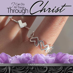 May include: Two silver rings on a finger. The top ring has a small square heart shape. The bottom ring has a series of connected heart shapes. The text "I Can Do All Things Through Christ" is at the top of the image.