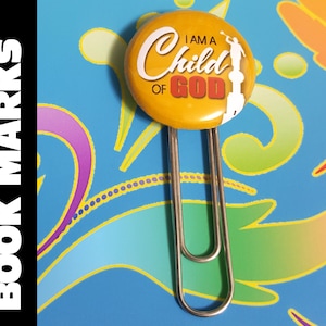 May include: A yellow bookmark with a silver metal clip. The bookmark has a round button with the text "I am a Child of God" in red and white lettering. A white silhouette of a person is on the right side of the button.