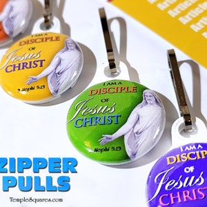 May include: A set of three zipper pulls featuring a colorful design with the text "I am a disciple of Jesus Christ" and a scripture reference. The zipper pulls are yellow, green, and purple.
