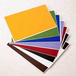 Op de afbeelding: Een waaier van rechthoekige kaarten in verschillende kleuren, waaronder geel, groen, blauw, paars, rood, zwart en bruin. Elke kaart heeft een witte rand. De kaarten zijn in een halve cirkel gerangschikt.