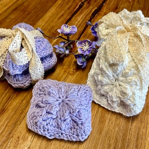 May include: Three crocheted lavender and white squares with a delicate lace trim. The squares are tied together with a white ribbon.