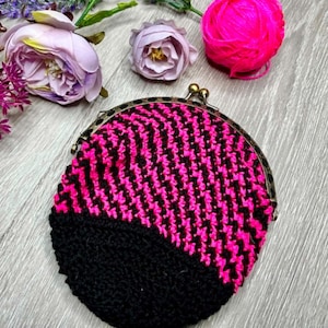 May include: A round crochet coin purse featuring a black and hot pink chevron pattern on the upper portion and a solid black base. The purse is secured with a metallic bronze-toned kiss-lock clasp frame at the top, providing a secure closure.