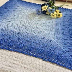 May include: A blue and white crocheted throw blanket with a lacy border. The blanket is made with a gradient yarn that transitions from white to blue.
