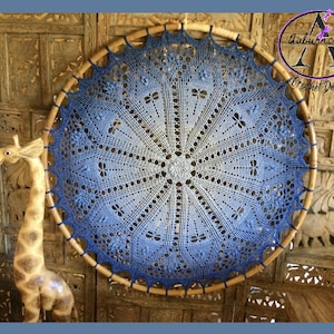 May include: A blue and white crocheted mandala with a gradient design hangs on a wooden wall. The mandala is circular and has a delicate lace pattern. The text "Auburncraft Crochet Design" is visible in the upper right corner of the image.