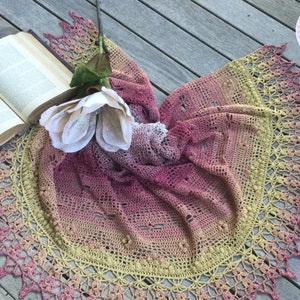 A delicate shawl featuring dragonflies and a intricate lace edge, laid out on a deck, with a flower and a book.