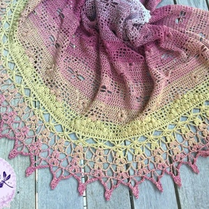 A delicate shawl featuring dragonflies and a intricate lace edge, laid out on a deck.