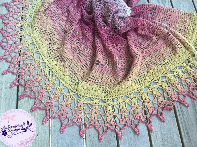 A delicate shawl featuring dragonflies and a intricate lace edge, laid out on a deck.