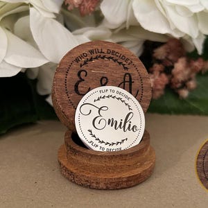 May include: A wooden box with a coin inside. The coin has the text "WHO WILL DECIDE?" and "FLIP TO DECIDE" on the top and bottom. The coin also has the name "Emilio" written on it. The box has the initials "E & A" engraved on the top.
