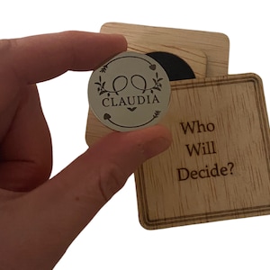 May include: A wooden box with a small metal coin inside. The coin has the name "CLAUDIA" engraved on it. The box has the text "Who Will Decide?" engraved on it.