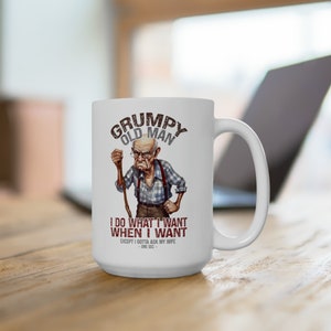 May include: White ceramic coffee mug with a cartoon illustration of a grumpy old man with a cane. The text reads "Grumpy Old Man I do what I want when I want except I gotta ask my wife -one sec-"
