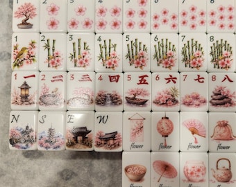 May include: A set of white Mahjong tiles featuring various illustrations including cherry blossoms, bamboo, dragons, lanterns, fans, and traditional Japanese architecture. Each tile displays a number or character, with some labeled as flower or joker.