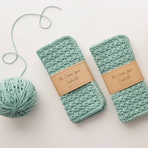 May include: Two light green linen dishcloths with brown labels that read "The Classic Linen Dishcloth Handmade with 100% Flax Cotton". A ball of light green yarn is in the background.