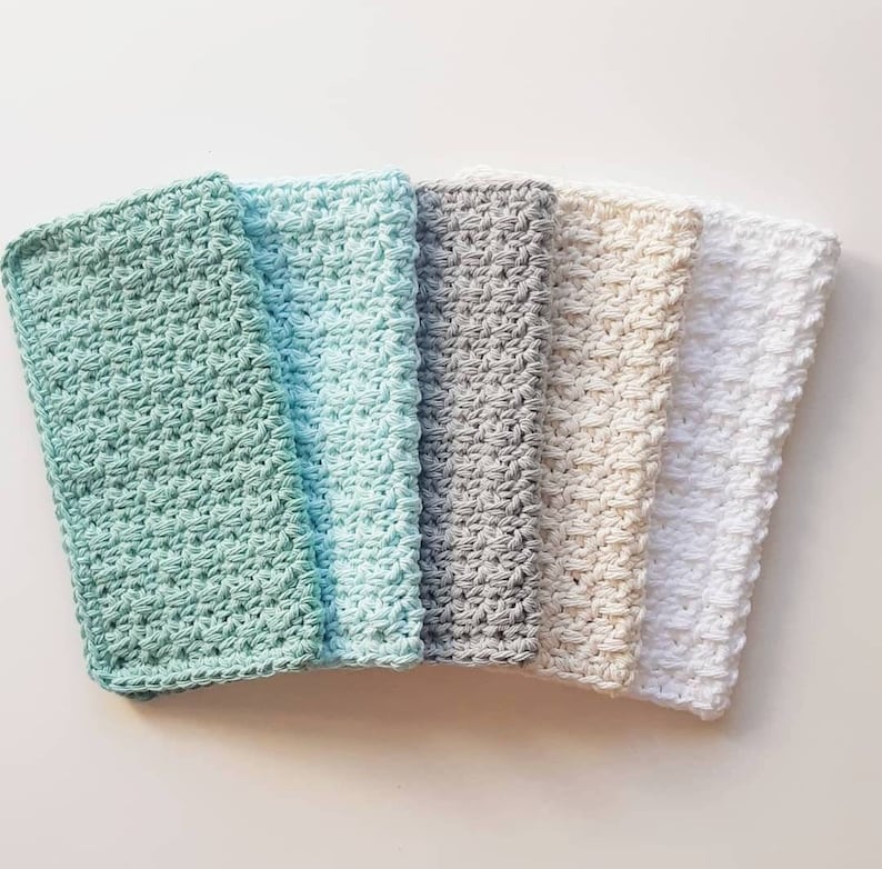 May include: Five crocheted dishcloths in different colours: light green, light blue, grey, beige, and white. The dishcloths are stacked on top of each other.