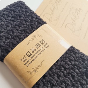 May include: A black crocheted dishcloth with a brown paper tag that says "Machine Wash and Dry on Gentle, Do Not Bleach / Iron / Dry Clean".