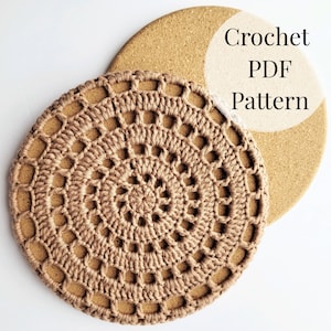 May include: A crocheted coaster in a light brown colour with a circular design. The coaster is on top of a cork trivet. The text "Crochet PDF Pattern" is written on the trivet.