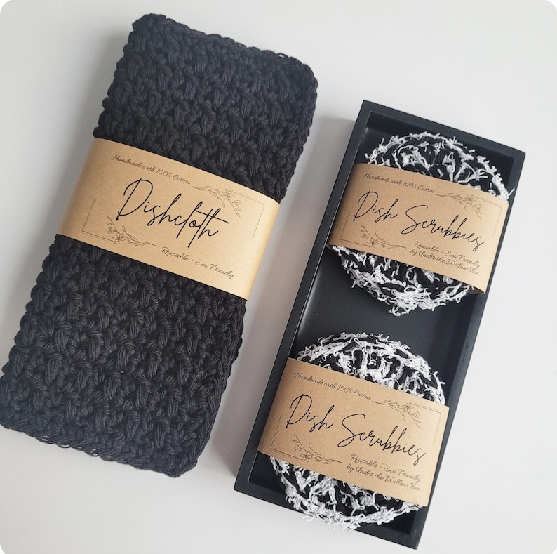 May include: A set of two black and white dish scrubbies and a black crocheted dishcloth. The scrubbies and dishcloth are handmade with 100% cotton and are reusable and eco-friendly. The scrubbies are packaged in a black wooden box with a label that reads "Dish Scrubbies Handmade with 100% Cotton Reusable - Eco Friendly by Under the Willow Tree". The dishcloth has a label that reads "Dishcloth Handmade with 100% Cotton Reusable - Eco Friendly".