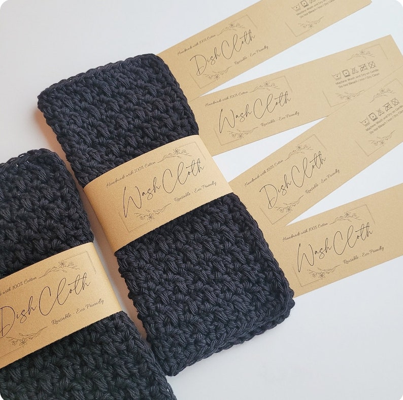 May include: Four brown paper tags with the text "Wash Cloth" and "Dish Cloth" in black cursive writing. The tags are attached to three black crocheted dishcloths.