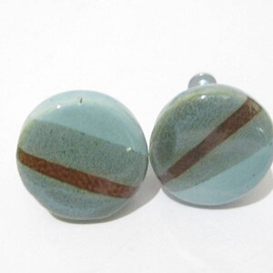 May include: Two ceramic cabinet knobs. Each knob is a light blue sphere with a diagonal brown stripe and a darker green stripe. The knobs are on a white background.