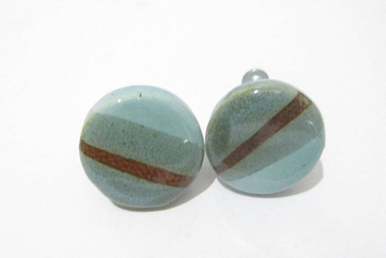 May include: Two ceramic cabinet knobs. Each knob is a light blue sphere with a diagonal brown stripe and a darker green stripe. The knobs are on a white background.