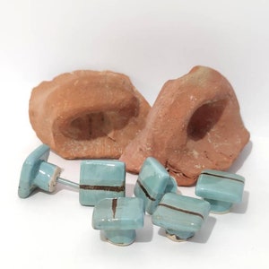 K&ouml;nnte beinhalten: Eine Sammlung hellblauer Keramik-Schrankkn&ouml;pfe mit einem dunkelbraunen Streifen, zusammen mit zwei Teilen r&ouml;tlich-brauner Keramik. Die Kn&ouml;pfe haben eine quadratische Form und sind an Metallschrauben befestigt.
