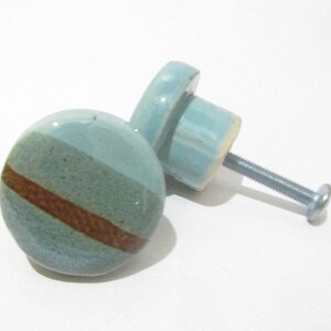 May include: Two ceramic cabinet knobs. The knobs are round with a light blue and brown striped design. Each knob has a metal screw for installation. The knobs are suitable for drawers or cabinets.