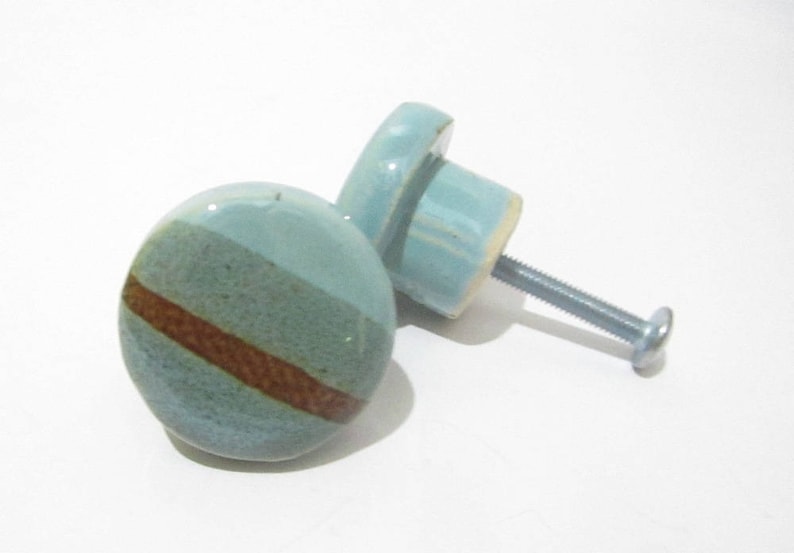 May include: Two ceramic cabinet knobs. The knobs are round with a light blue and brown striped design. Each knob has a metal screw for installation. The knobs are suitable for drawers or cabinets.