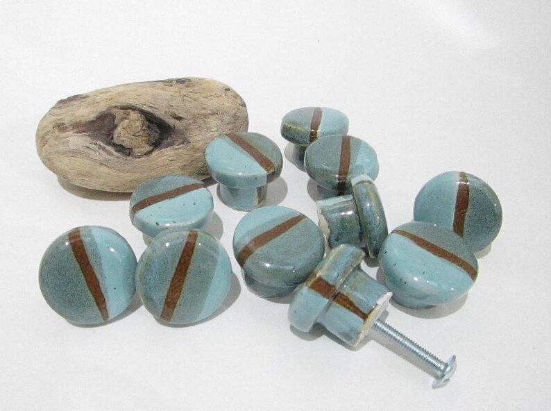 May include: A selection of ceramic cabinet knobs in teal and brown. Each knob has a teal base with a diagonal brown stripe. The knobs are round and cylindrical, with a screw for attachment. A piece of driftwood is also present.