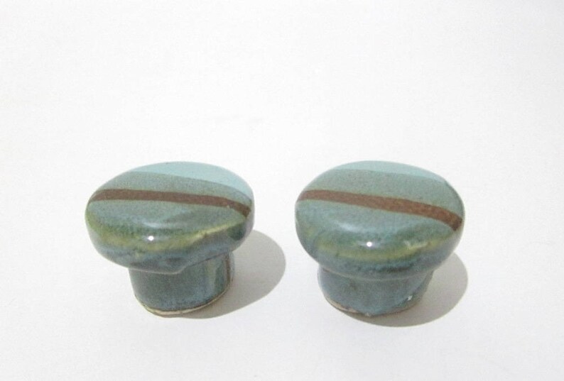 May include: Two ceramic cabinet knobs. Each knob is a rounded shape with a teal and brown stripe design. The knobs have a glossy finish and are set against a white background.