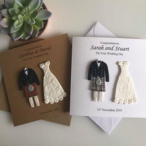 K&ouml;nnte beinhalten: Zwei Hochzeitskarten, eine braun-wei&szlig; und eine wei&szlig;e. Die Karten zeigen eine Braut und einen Br&auml;utigam in traditioneller schottischer Tracht. Der Text auf den Karten lautet "Herzlichen Gl&uuml;ckwunsch Caroline & David Zu Ihrem Hochzeitstag" und "Herzlichen Gl&uuml;ckwunsch Sarah und Stuart Zu Ihrem Hochzeitstag".
