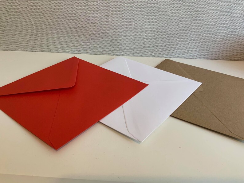 May include: Three square envelopes arranged in a row, featuring one vibrant red envelope, one crisp white envelope, and one natural brown kraft paper envelope. Each envelope is closed with a triangular flap pointing towards the centre.