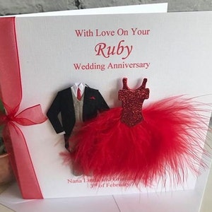 May include: A white card with red ribbon and red feathers. The card has the text "With Love On Your Ruby Wedding Anniversary".