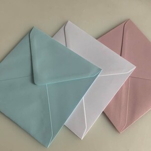Pu&ograve; includere: Tre buste quadrate di diversi colori: azzurro, bianco e rosa chiaro. Le buste sono piegate e impilate l'una sull'altra.