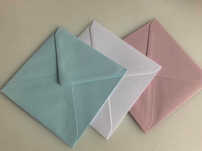 Pu&ograve; includere: Tre buste quadrate di diversi colori: azzurro, bianco e rosa chiaro. Le buste sono piegate e impilate l'una sull'altra.