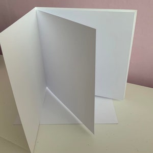 May include: A white card folded in half, with the inside of the card facing the camera. The card is blank.