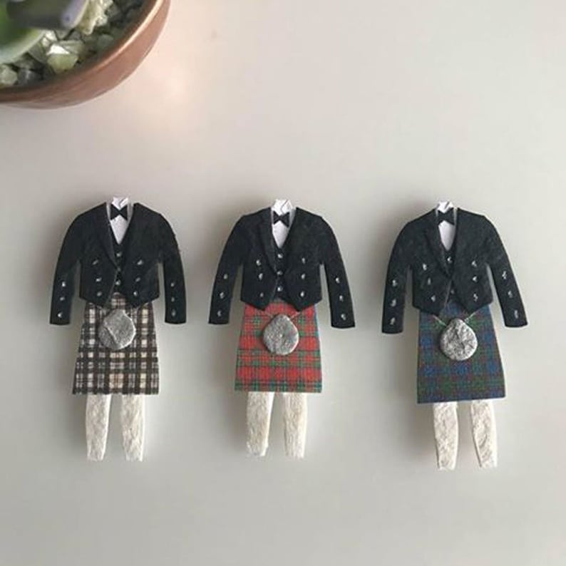 K&ouml;nnte beinhalten: Drei Papierschnitte von M&auml;nnern in traditionellen schottischen Kilts. Jeder Kilt hat ein anderes Tartanmuster: Braun und Wei&szlig;, Rot und Gr&uuml;n sowie Blau und Gr&uuml;n. Jeder Mann tr&auml;gt eine schwarze Jacke mit einem wei&szlig;en Hemd und einer schwarzen Fliege.
