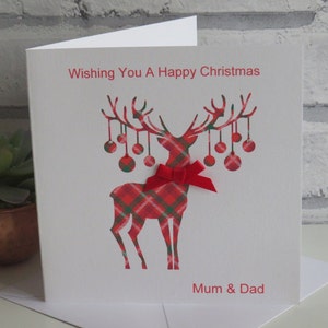 May include: A white greeting card featuring a red and green plaid reindeer silhouette with hanging ornaments on its antlers. A red ribbon bow is attached to the reindeer's neck. The text reads Wishing You A Happy Christmas and Mum & Dad.
