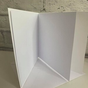 Pu&ograve; includere: Un biglietto bianco piegato a met&agrave;, con l'interno e l'esterno vuoti. Il biglietto &egrave; piegato in modo da creare una forma triangolare al centro.