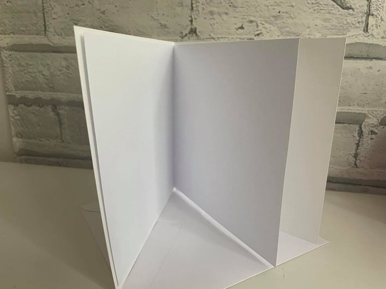 Pu&ograve; includere: Un biglietto bianco piegato a met&agrave;, con l'interno e l'esterno vuoti. Il biglietto &egrave; piegato in modo da creare una forma triangolare al centro.