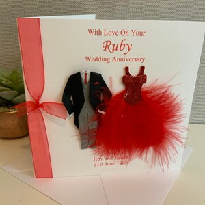 May include: A white card with a red ribbon and a red feather boa. The card says "With Love On Your Ruby Wedding Anniversary" and "Roy and Janice 21st June 1980".